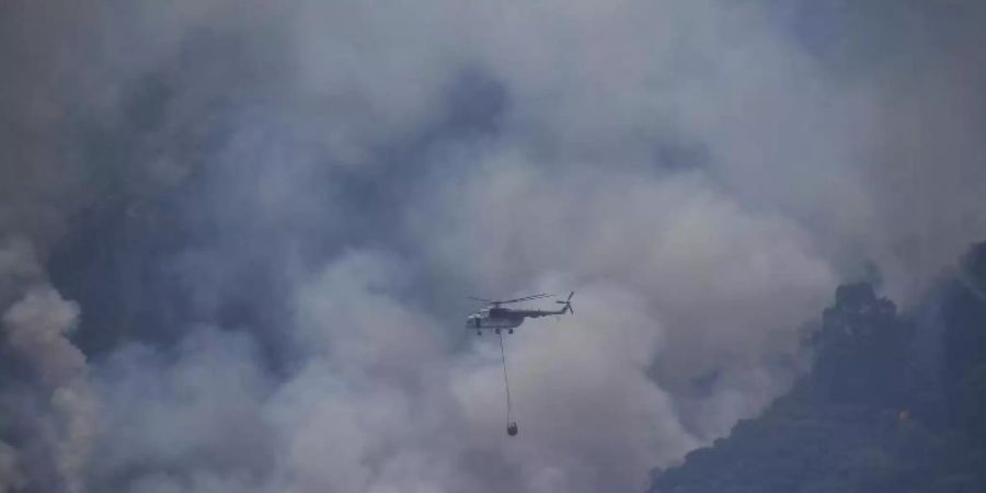 Ein Hubschrauber transportiert im türkischen Turgut Löschwasser zu einem Waldbrand. Foto: Emre Tazegul/AP/dpa