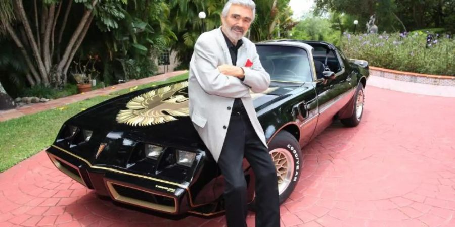 Schauspielers Burt Reynolds steht an seinem schwarz-goldenen Sportwagen der Marke Pontiac Trans Am (1979). Das Auto gehört zu Filmmemorabilien, Kleidungsstücken und Möbeln aus dem Privatbesitz des Schauspielers, die am 15. und 16. Juni in Beverly Hills versteigert werden. Foto: Juliens Auctions