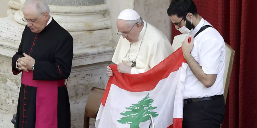 Papst Franziskus (M) hält bei seiner ersten Generalaudienz mit Gläubigen seit Ausbruch der Corona-Pandemie in Gedenken an die Opfer der Explosion die Flagge des Libanon. Foto: Andrew Medichini/AP/dpa