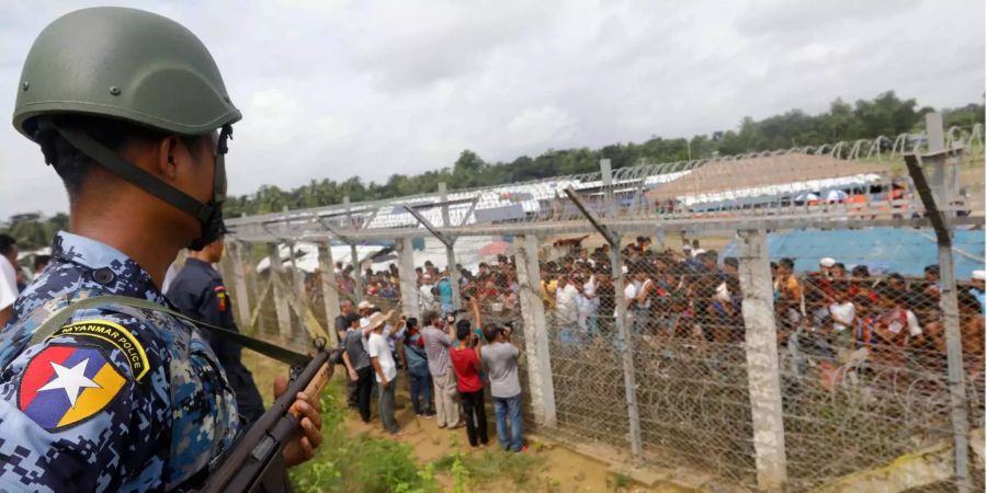 Ein Grenzpolizist steht neben einem Zaun Wache. Hinter dem Zaun stehen Rohingyas und behelfsmässig errichtete Hütten in der Niemandsland-Zone in der Bangladesh-Myanmar-Grenze in Maungdaw, Rakhine-Staat.