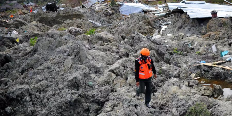 Ein indonesisches Such- und Rettungsteam, sucht ein, von getrocknetem Schlamm überzogenes, Gebiet auf Sulawesi, ab.