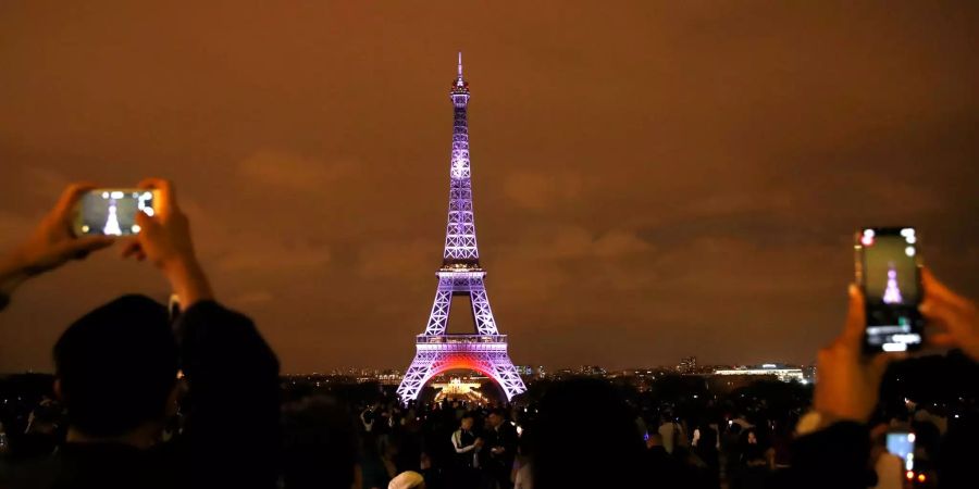 Touristen fotografieren den Eiffelturm in Paris, der im Rahmen des Besuchs des japanischen Kronprinzen Naruhito in Frankreich beleuchtet wurde.