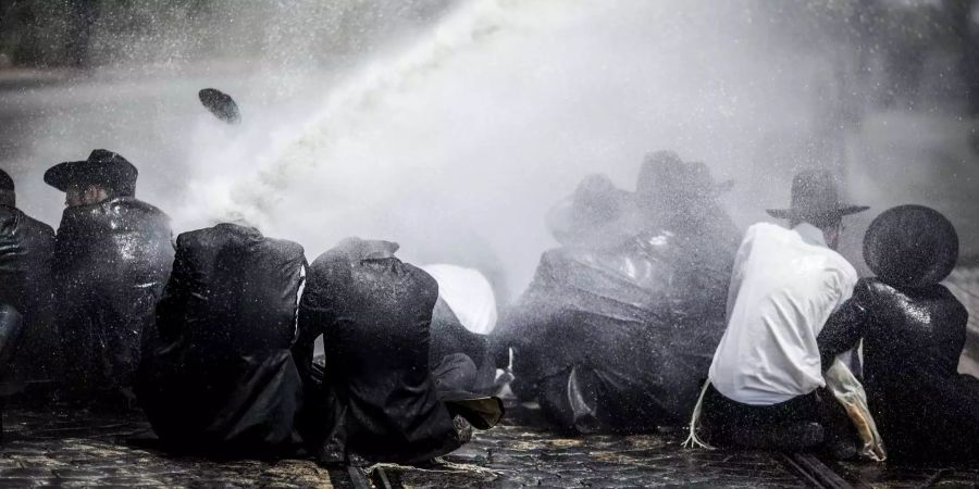 Die jüdische Männer werden von der israelischen Polizei mit Wasser aus einer Wasserkanone besprüht