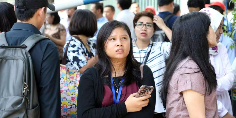 Menschen stehen auf der Strasse, nachdem sie in Jakarta (Indonesien) bei einem Erdbeben aus einem Hochhaus evakuiert wurden.