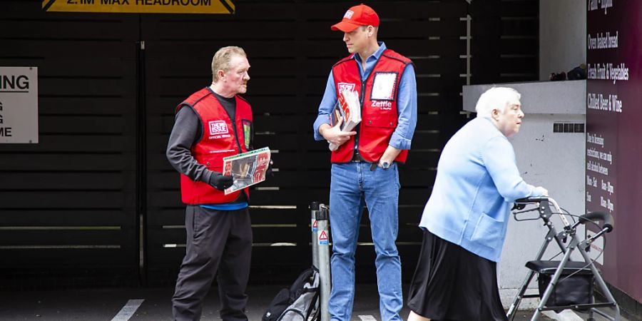 HANDOUT - Prinz William (M), Herzog von Cambridge hilft dem Big Issue-Verkäufer Dave Martin (l) beim Verkauf des Magazins. Die Strassenzeitung hat es sich zum Ziel gesetzt obdachlosen, langzeitarbeitslosen und ausgegrenzten Menschen die Möglichkeit zu geben, ein Einkommen zu erzielen. Foto: Andy Parsons/The Big Issue/PA Media/dpa - ACHTUNG: Nur zur redaktionellen Verwendung und nur mit vollständiger Nennung des vorstehenden Credits