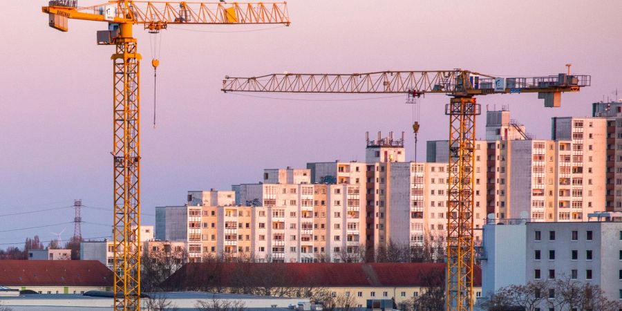 Baukräne leuchten vor einer Wohnsiedlung golden im Licht der aufgehenden Sonne in Berlin.