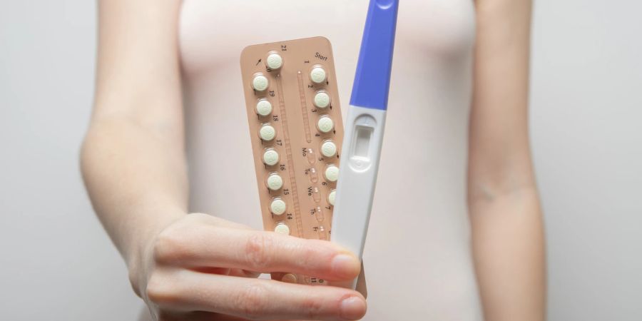 Eine Person hält die Pillenpackung und einen Schwangerschaftstest