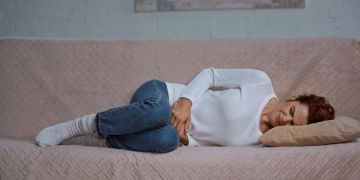 Frau liegt mit bauchkrämpfen auf dem Sofa.