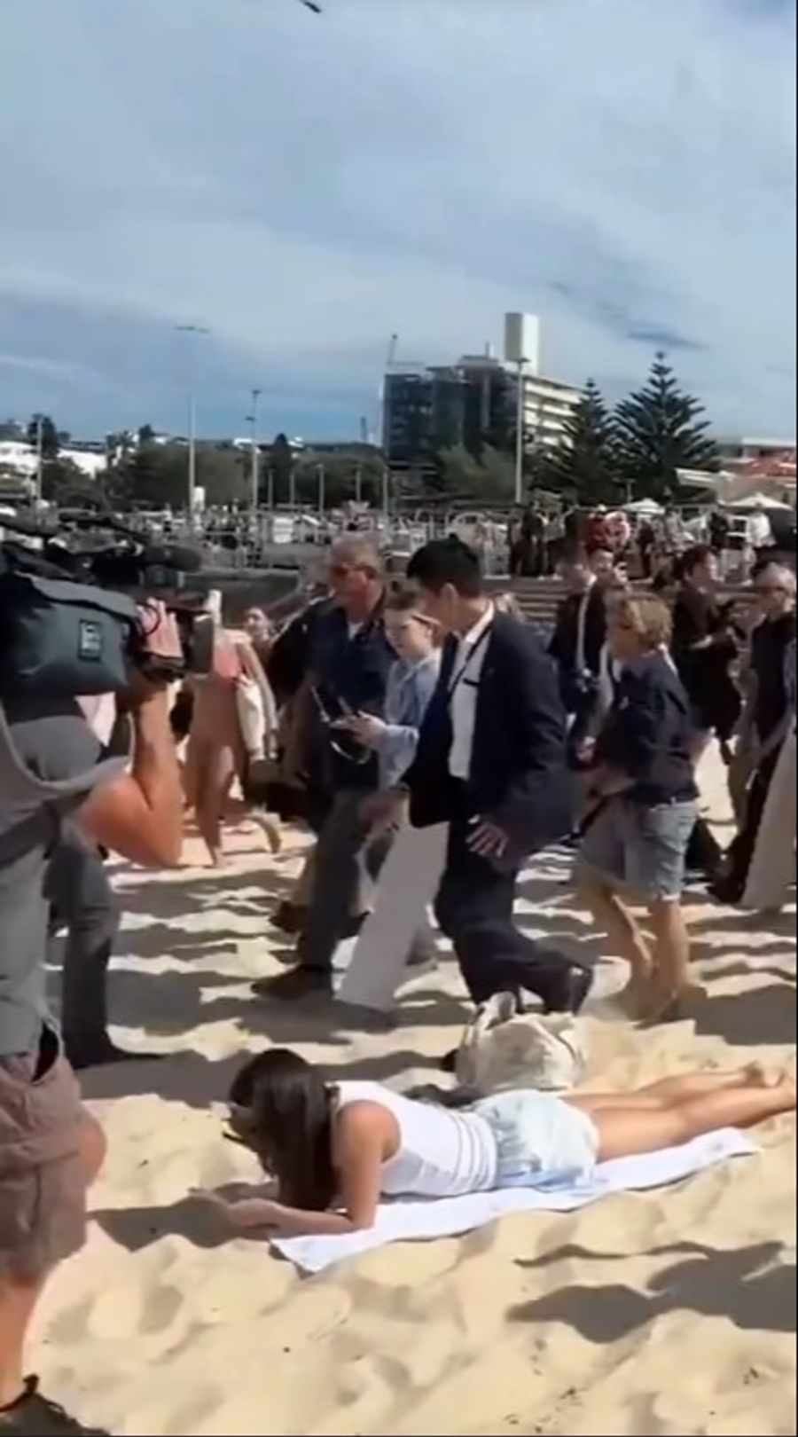 Während Harry und Meghan am Bondi Beach vorbeiziehen, bleibt eine Strandbesucherin einfach liegen und liest weiter.