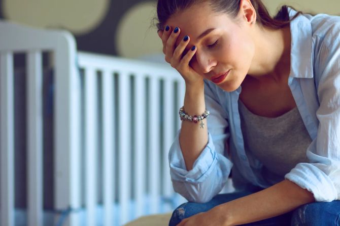 Überforderte, nachdenkliche Frau sitzt vor einem Kinderbett
