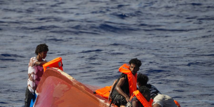 ARCHIV - Migranten helfen einander südlich der italienischen Insel Lampedusa im Mittelmeer, auf ihr gekentertes Holzboot zu klettern. Foto: Francisco Seco/AP/dpa
