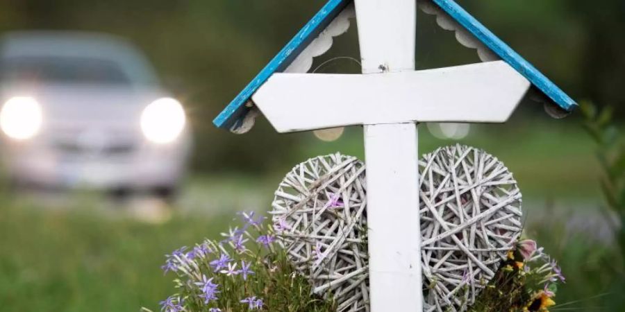 Autos fahren an einem weissen Kreuz für eine Unfalltote vorbei. Im ersten Quartal 2019 sind auf deutschen Strassen 633 Menschen gestorben. Foto: Sebastian Gollnow/Archiv