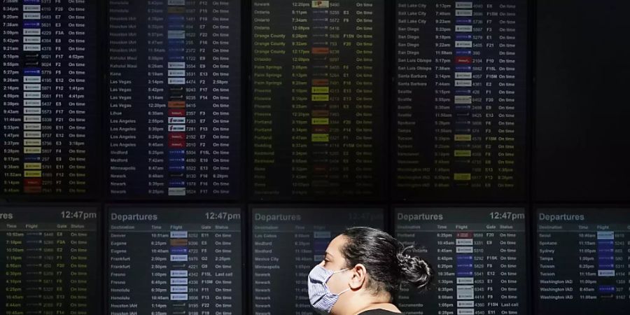 ARCHIV - Eine Frau mit Mund-Nasen-Schutz geht an einer Anzeigetafel am Internationalen Flughafen von San Francisco vorbei. Foto: Jeff Chiu/AP/dpa