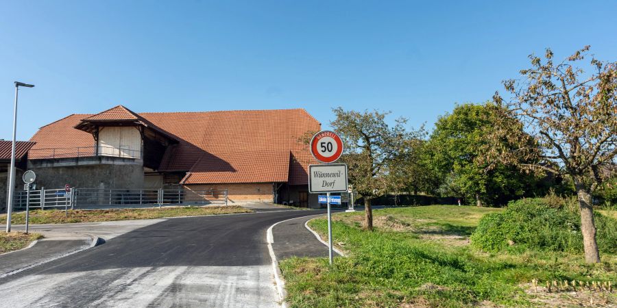 Das Dorfschild von Wünnewil-Dorf und ein Bauernhaus.