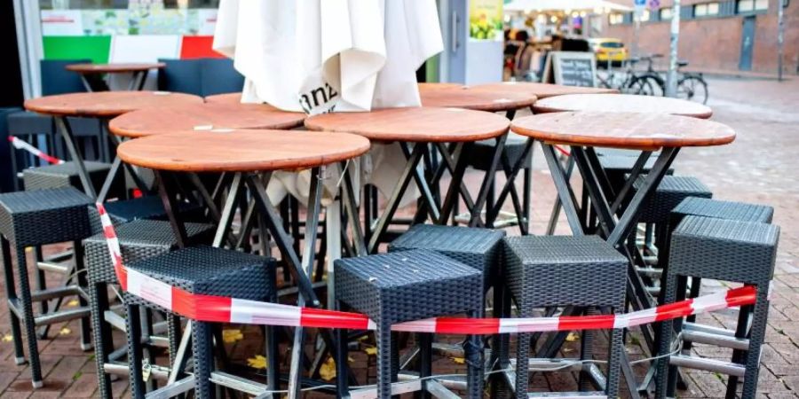 Derzeit keine Einnahmen: Mit Flatterband abgesperrte Tische und Stühle stehen vor einer Pizzeria in der Corona-Pandemie. Foto: Hauke-Christian Dittrich/dpa