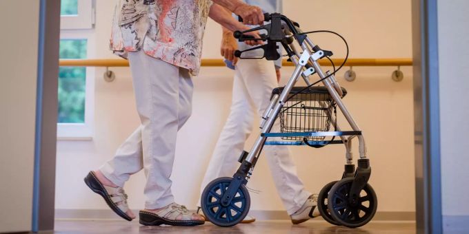 Eine Pflegekraft geht in einem Pflegeheim mit einer älteren Dame über einen Korridor. Coronavirus