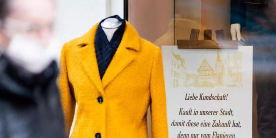 Eine Person mit Mund-Nasen-Schutz geht am Schaufenster eines Bekleidungsgeschäfts vorbei. Foto: Christoph Soeder/dpa/Archivbild