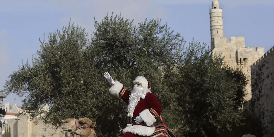 Ein Mann in einem Weihnachtsmann-Kostüm sitzt auf einem Kamel ausserhalb der Altstadt von Jerusalem. Foto: Mahmoud Illean/AP/dpa