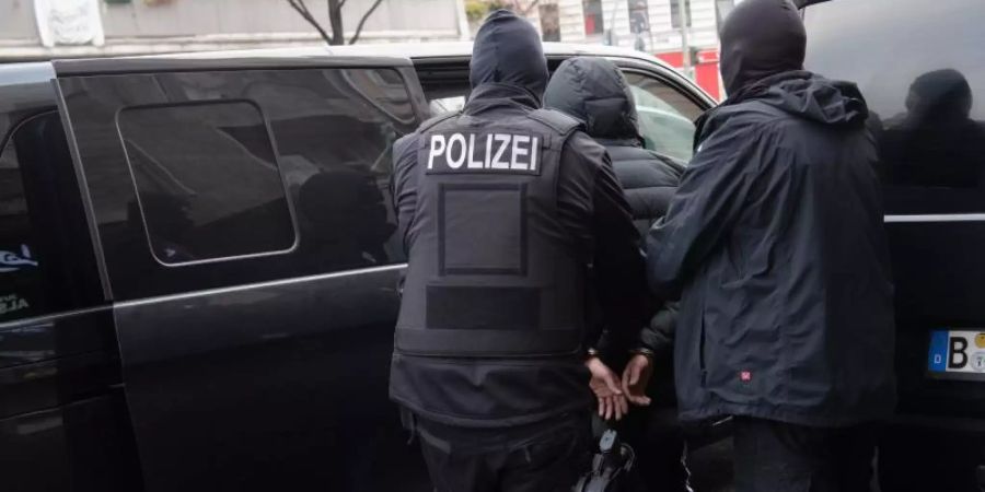 Polizisten führen einen Mann ab. Die Durchsuchungen stehen den Angaben zufolge im Zusammenhang mit Ermittlungen wegen des Verdachts der gewerbsmässigen Hehlerei und der gewerbsmässigen Geldfälschung. Foto: Paul Zinken/dpa