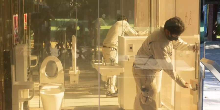 Ein Mann schliesst die Tür einer neu installierten öffentlichen Toilette mit transparenten Wänden, die im Yoyogi Fukamachi Mini Park im Bezirk Shibuya steht. Die drei Toiletten aus transparentem Glas werden undurchsichtig, sobald jemand eintritt und die Tür verschliesst. Foto: Rodrigo Reyes Marin/ZUMA Wire/dpa