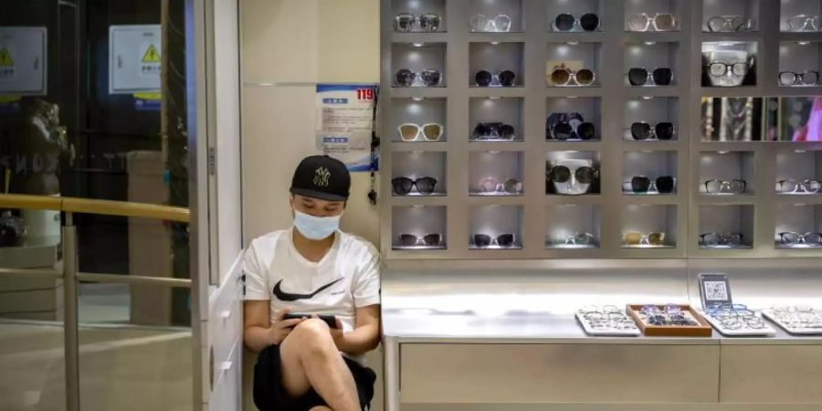 Ein Mitarbeiter mit Mundschutz wartet in einem Geschäft in Peking auf Kunden. Der Umsatz im chinesischen Einzelhandel ging im Juli um 1,1 Prozent zurück. Foto: Mark Schiefelbein/AP/dpa