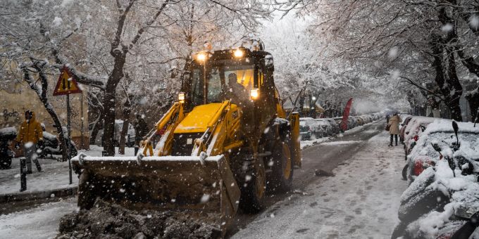 Ein Radlader ist bei Schneefall im Einsatz, um mit seiner Baggerschafel Schnee und Eis von einer Strasse zu schieben. Schnee in Griechenland