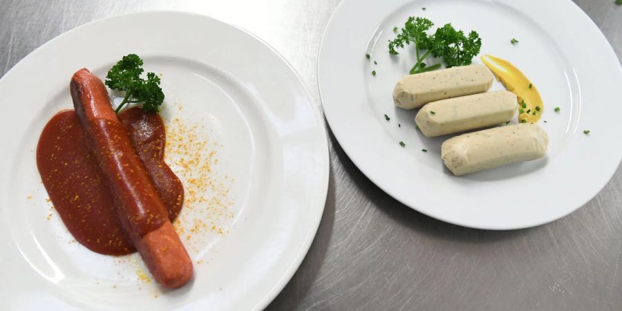 Eine vegane Currywurst und vegane Weisswürste liegen auf Tellern an der Essensausgabe im Hofbräuzelt auf dem Oktoberfest.