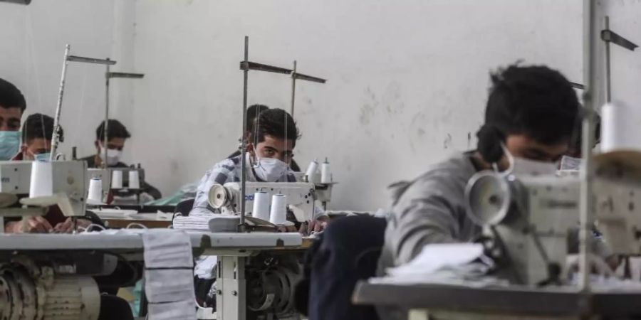 Arbeiter in der umkämpften Region Idlib mit Gesichtsmasken. In einem kleinen Labor stellen sie notdürftig Schutzmasken her. Foto: Anas Alkharboutli/dpa