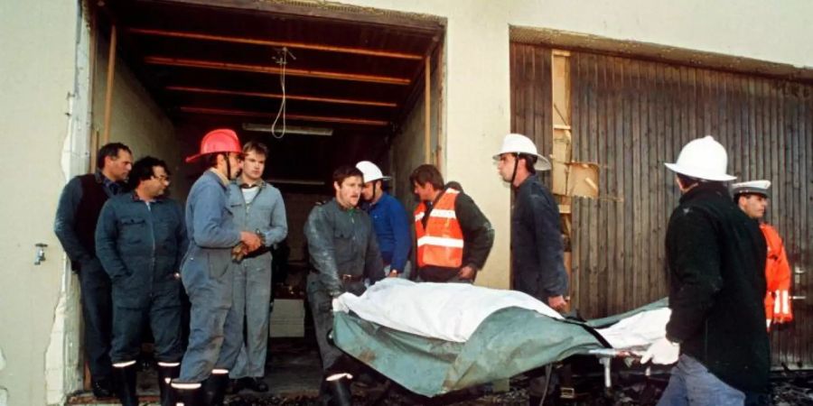 Polizei und Feuerwehrleute tragen am 5. Oktober 1994 die tot aufgefundenen Sektenmitglieder aus dem Haus in Cheiry im Kanton Freiburg. Hier starben zehn Männer, zwölf Frauen und ein Kind. Foto: Keystone/epa