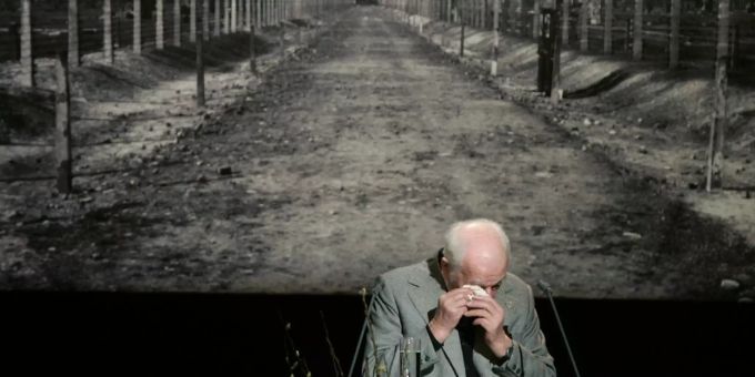 Ein Holocaust-Überlebender vor einem Bild von Auschwitz (Symbolbild). Nazi Hitler Holocaust