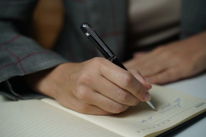Ein Erfolgstagebuch kann bei Stressbewältigung helfen. Hand Kugelschreiber Tagebuch