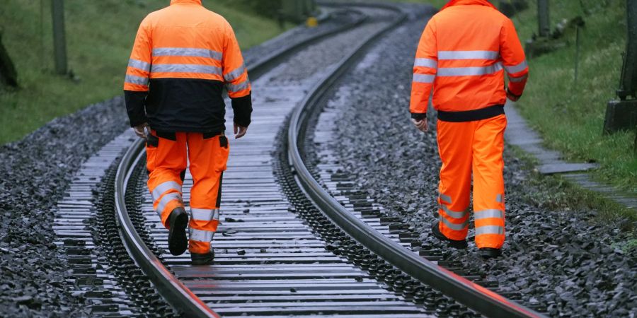 SBB Mitarbeiter (Gleisbauer) laufen an Zug Geleisen entlang.