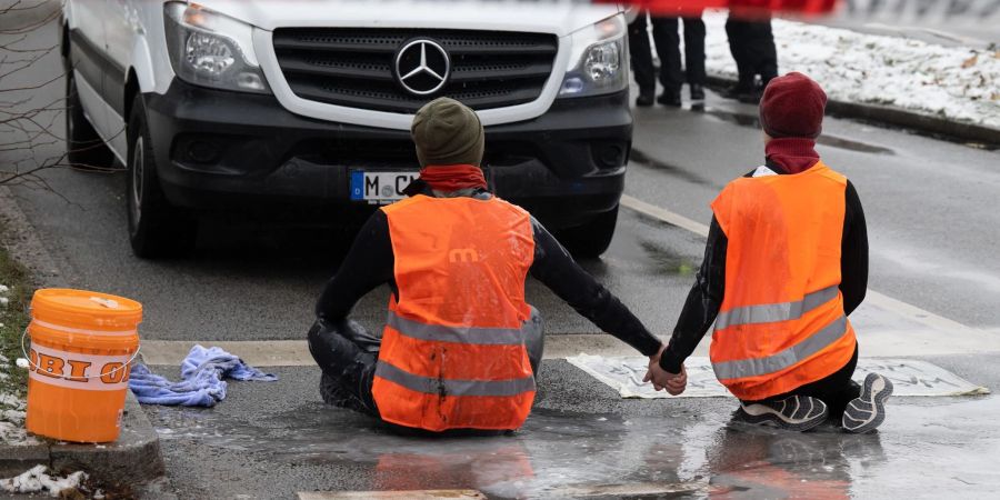 Zwei Klimaaktivisten der «Letzten Generation» versuchen, sich auf einer Strasse in München trotz Nieselregen und Minusgraden festzukleben.