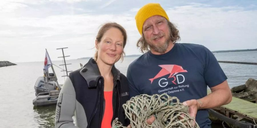 Das Schauspieler-Paar Tessa Mittelstaedt (47) und Matthias Komm (54) steht vor einem Tauchgang in die Ostsee vor der Insel Rügen an der Tauchbasis Mukran mit einem Netz in der Hand da. Foto: Stefan Sauer/dpa