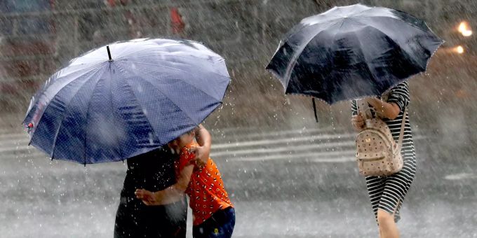 Fussgänger gehen mit Schirmen bei regnerischem Wetter über einen Fussgängerstreifen. (Symbolbild) tessin überschwemmungen