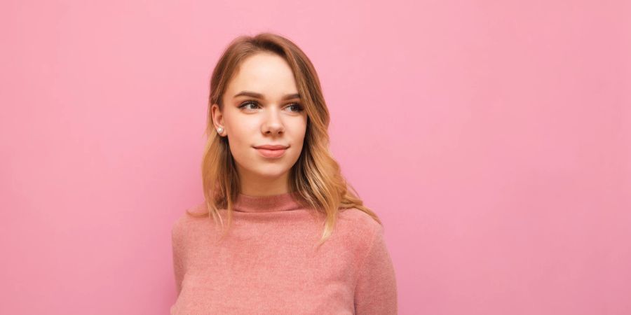 Junge Frau mit honigblondem Haar und rosafarbenem Pullover