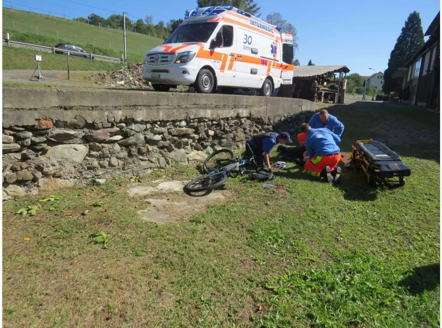 Fahrrad neben einer Strasse am Boden und daneben Rettungskräfte, die sich um den Fahrradlenker kümmern - zvg Kantonspolizei Aargau