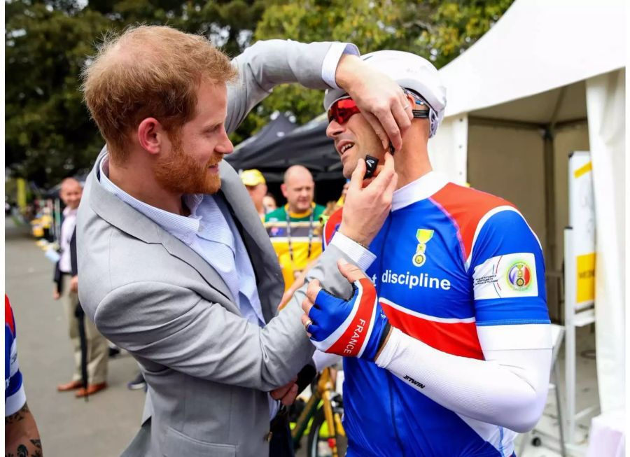 Der britische Prinz Harry (l) hilft bei den der Invictus Games 2018 einem Teilnehmer den Helm aufzusetzen.