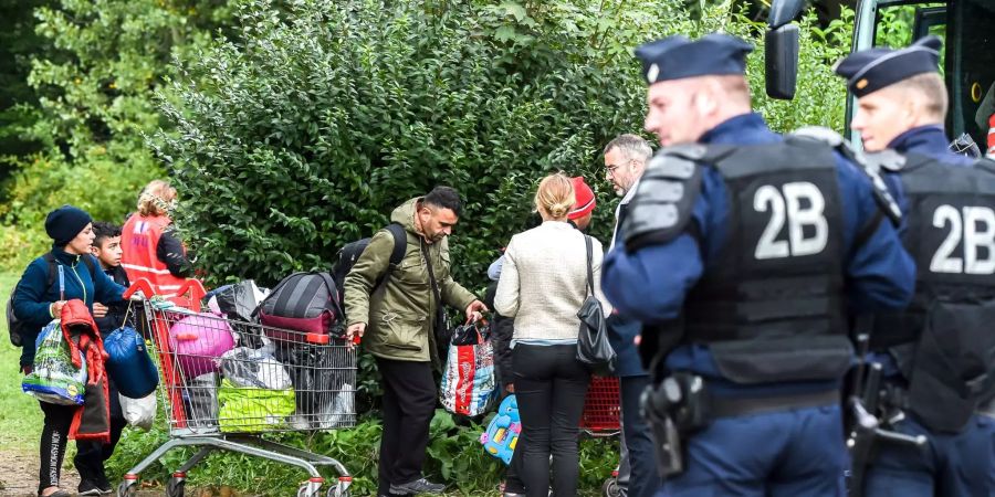 Französische Polizisten (r) beobachten, wie Menschen das  Flüchtlingslager in Grande-Synthe bei Dünkirchen  verlassen.