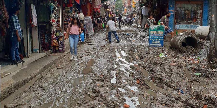 Passanten gehen über eine schlammige Strasse nach Regenfällen in der nepalesischen Hauptstadt Kathmandu.