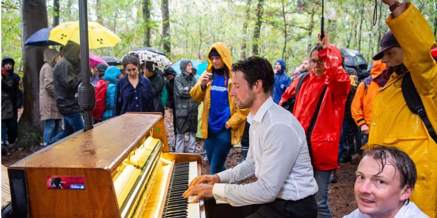 Ein Teilnehmer der Demonstration gegen die Rodung des Hambacher Forsts sitzt im Wald und spielt im Regen Klavier.