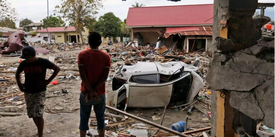 Männer betrachten die Schäden in einem vom Tsunami verwüsteten Gebiet in Palu (IND).