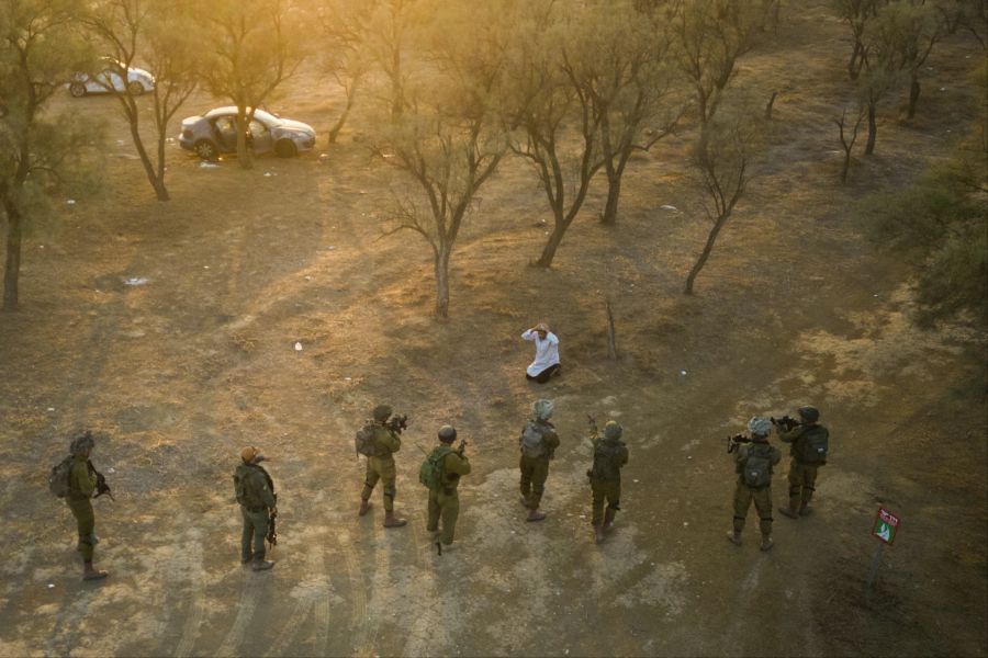 Israelische Soldaten umrunden einen Hamas-Kämpfer, der sie mit einem Messer angriff. Davor töteten Hamas auf dem Festivalgelände im Hintergrund mindestens 260 Feiernde.