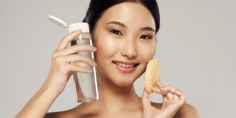 Reinigung Gesicht asiatische Frau mit Schwamm und Wasserflasche.