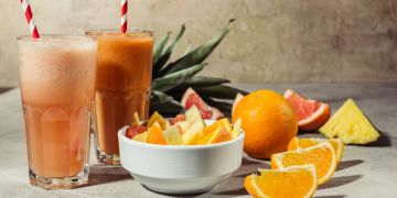 Orangensaft in einem Glas und Orangenschnitze in einer Schale und auf dem Tisch.