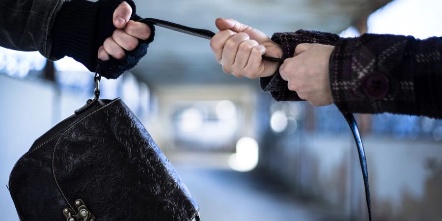 Männerarm und Frauenarm im Kampf um eine Handtasche.