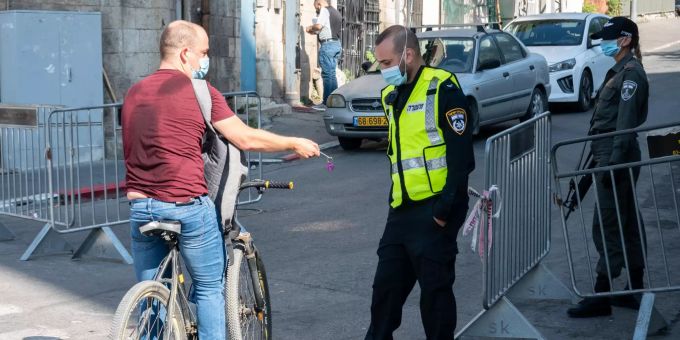 Ein Polizist (r) lässt sich von einem Radfahrer den Ausweis zeigen. Die Polizei setzt aufgrund erneut steigender Infektionszahlen während der Corona-Pandemie eine Abriegelung des vorwiegend jüdisch-religiösen Viertels Romema in Jerusalem sowie weiterer Viertel in 5 Städten im ganzen Land durch. Coronavirus- Israel