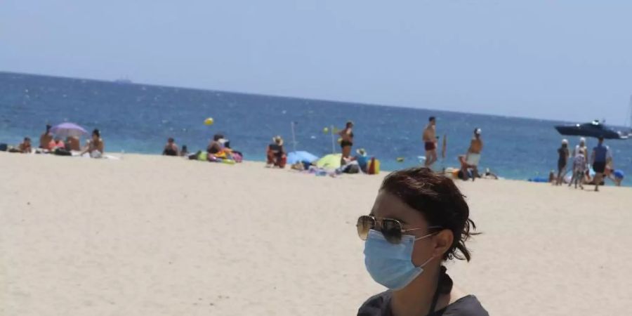 Eine junge Frau mit einer Schutzmaske an einem Strand. Foto: Clara Margais/dpa
