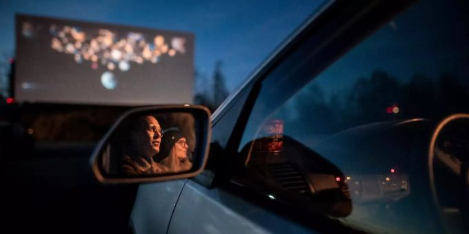 Zwei Besucher eines Autokino sitzen im Auto und gucken auf die Leinwand. Auto-Kino