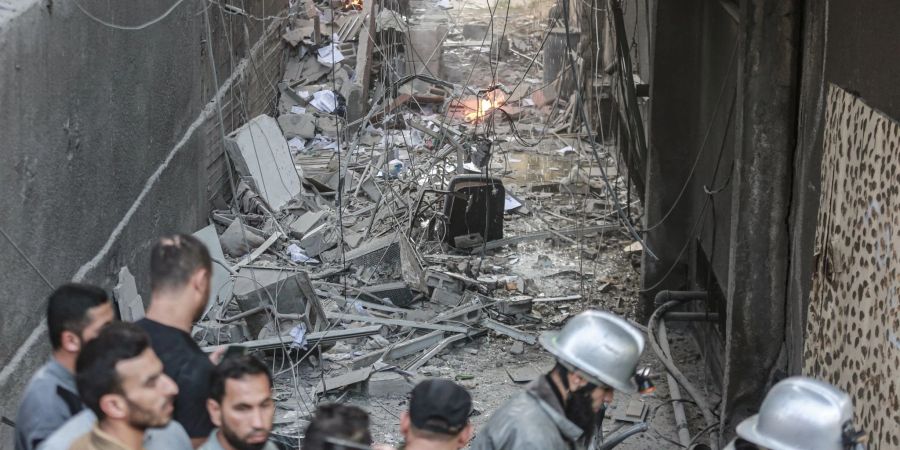 Männer und zwei Feuerwehrleute stehen nach einem israelischen Luftangriff vor Trümmern. Bei Angriffen des israelischen Militärs auf den Gazastreifen sind palästinensischen Angaben zufolge mehrere Menschen getötet worden.